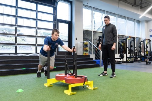 Man pushing weighted sled in gym training session.