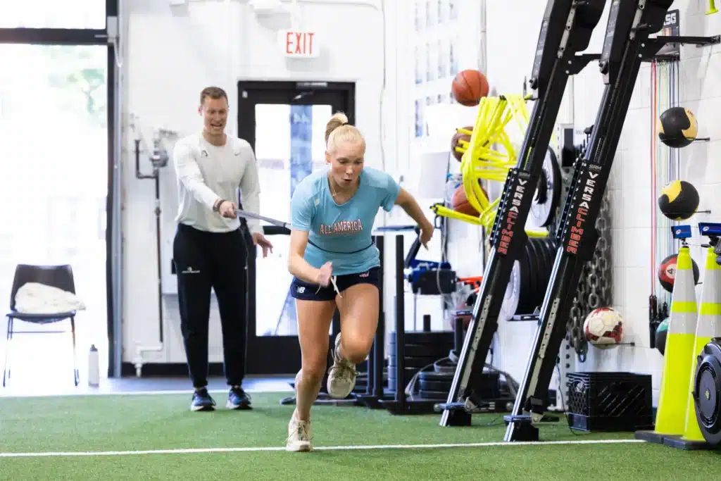Athlete training indoors with coach's guidance on turf.