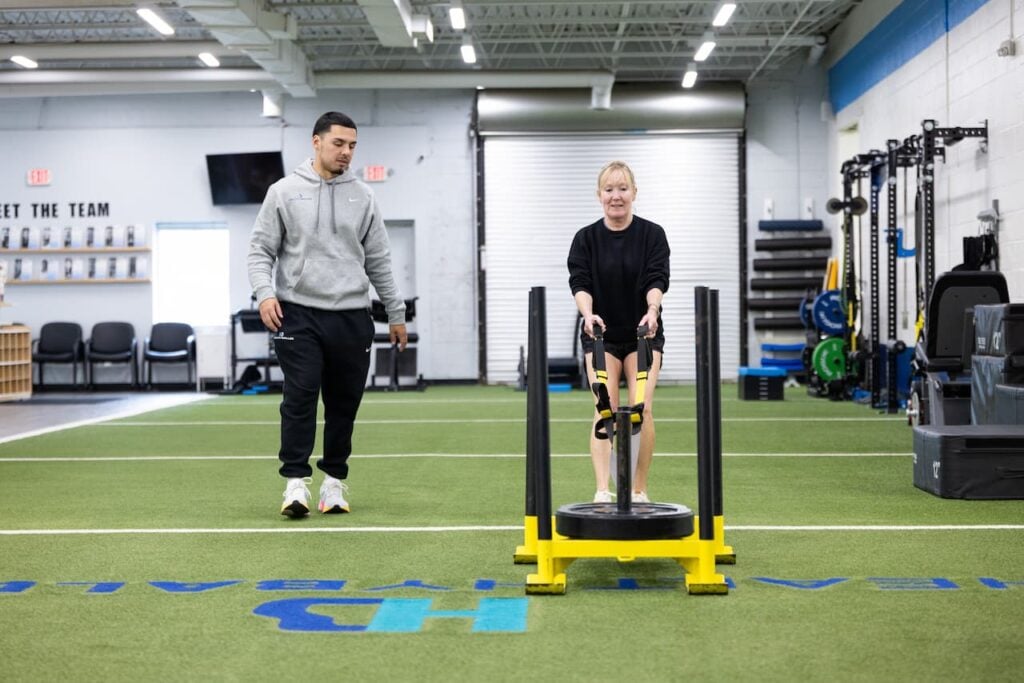 Trainer guiding woman pushing sled in gym.