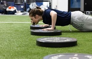 Woman doing push-ups over gym weights indoors.