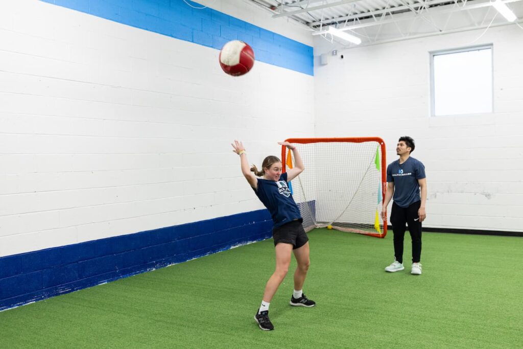 Woman playing dodgeball indoors with coach observing