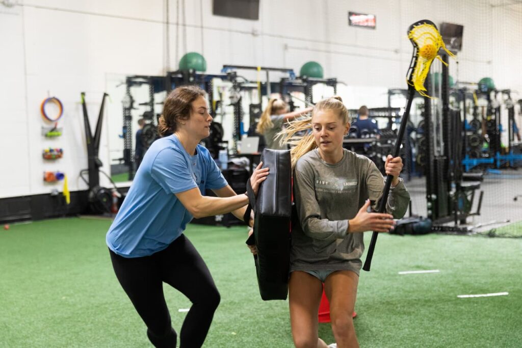 Lacrosse players training indoors with equipment.