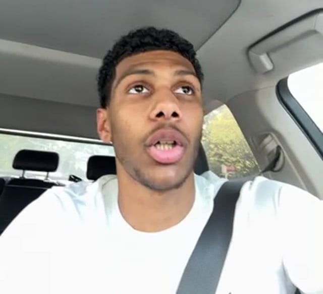 Person driving a car, wearing a white shirt.