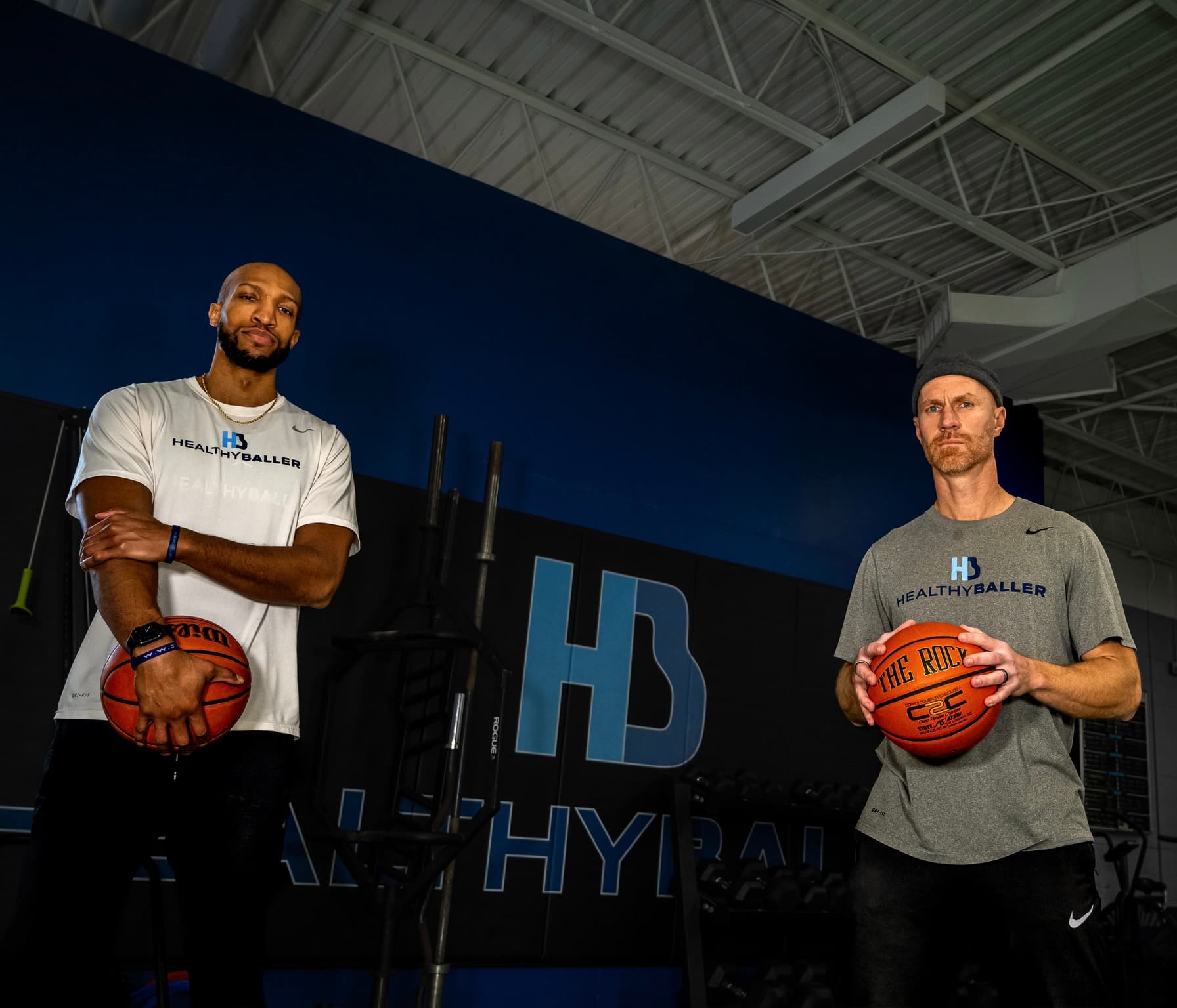 Two men with basketballs in a gym setting.