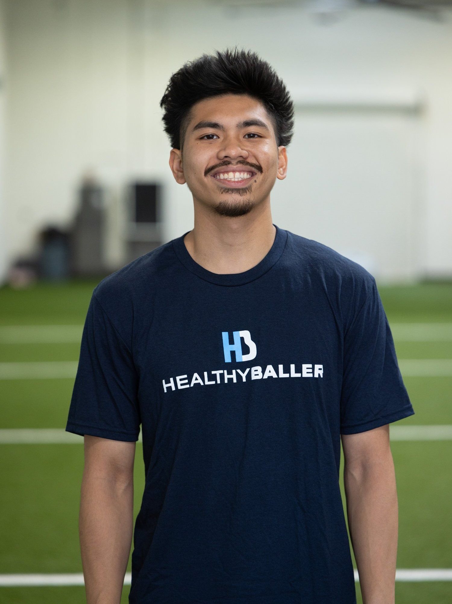 Person smiling wearing Healthy Baller shirt indoors.