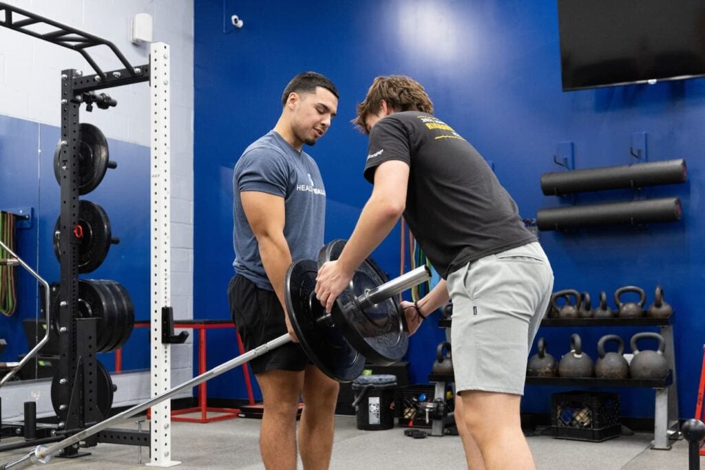 Two men lifting weights in gym setting.