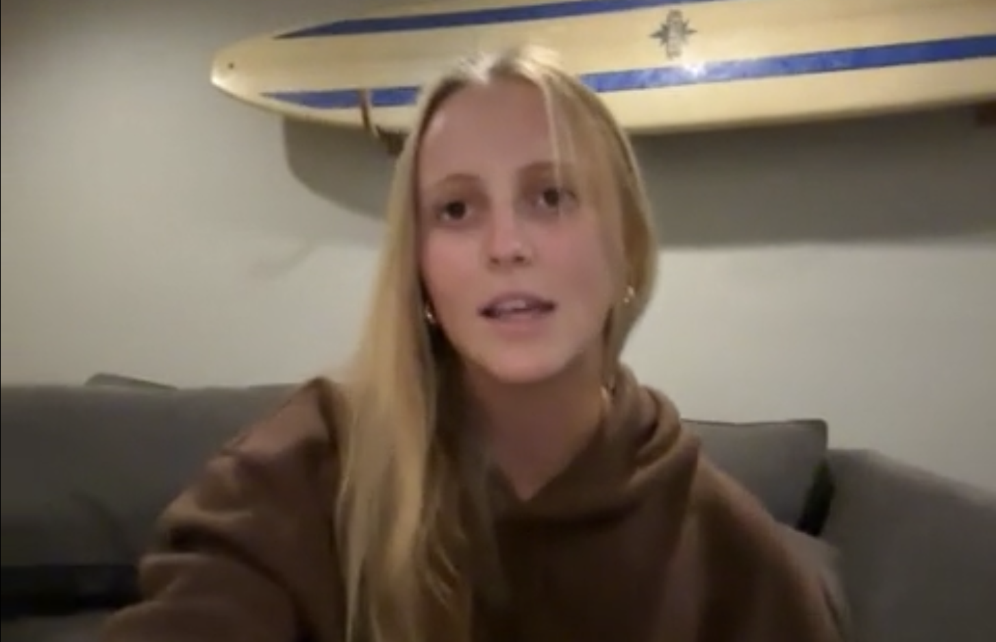 Person speaking in room with surfboard on wall.