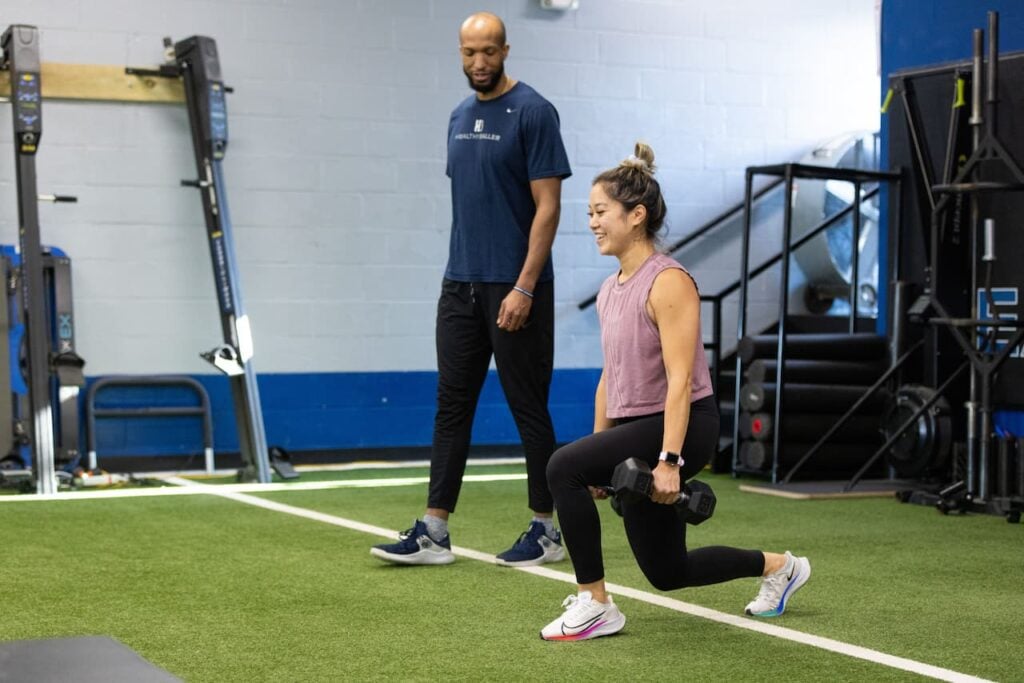 Woman doing lunges with trainer at gym.