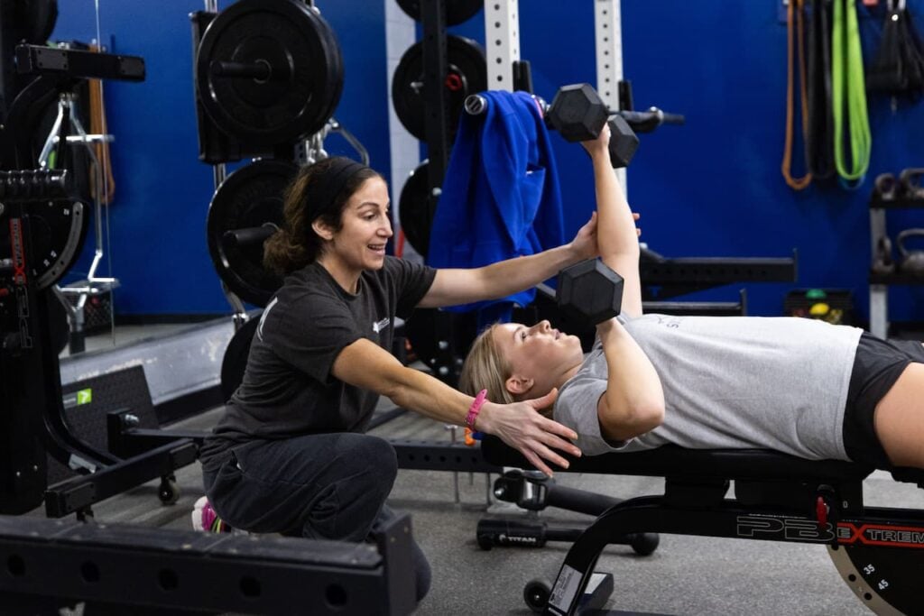 Personal trainer guides client in dumbbell exercise.