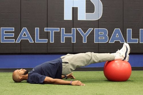 Man exercising with stability ball on gym floor.