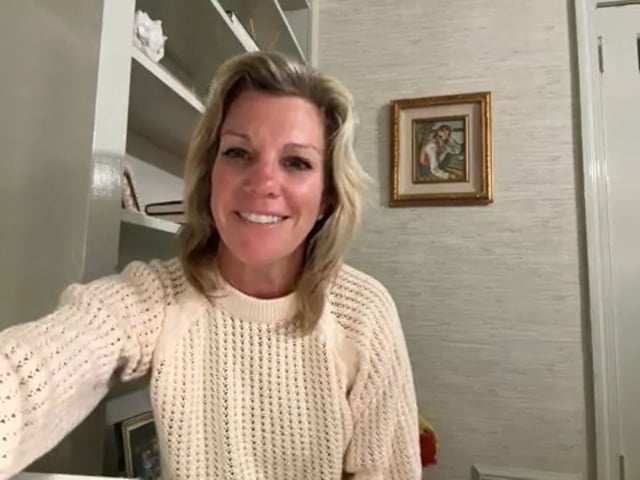 Woman smiling indoors near bookshelf and painting.