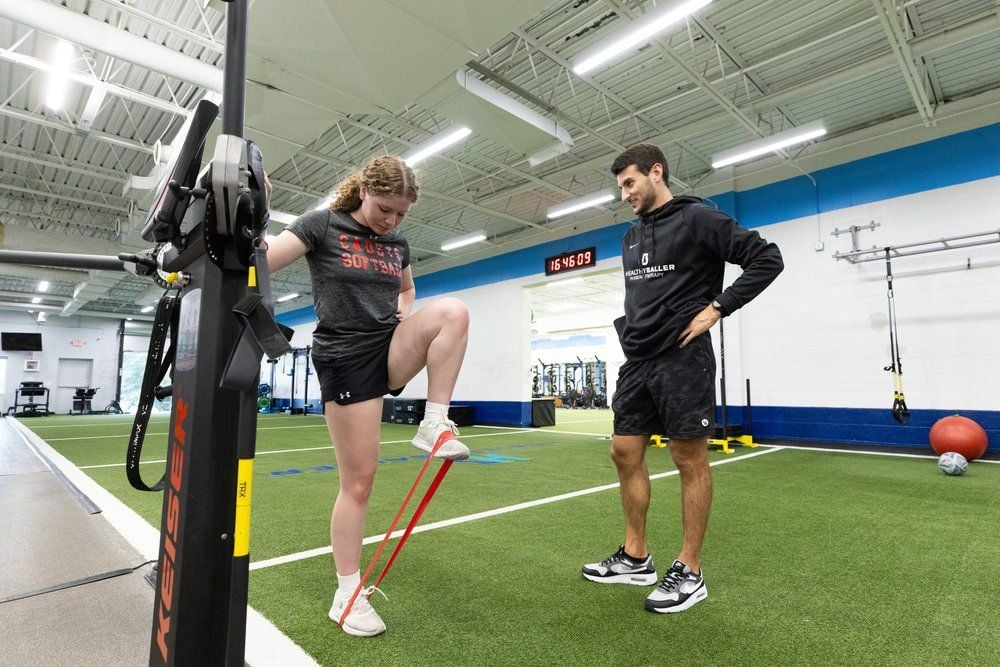 Trainer supervising woman exercising with resistance bands.