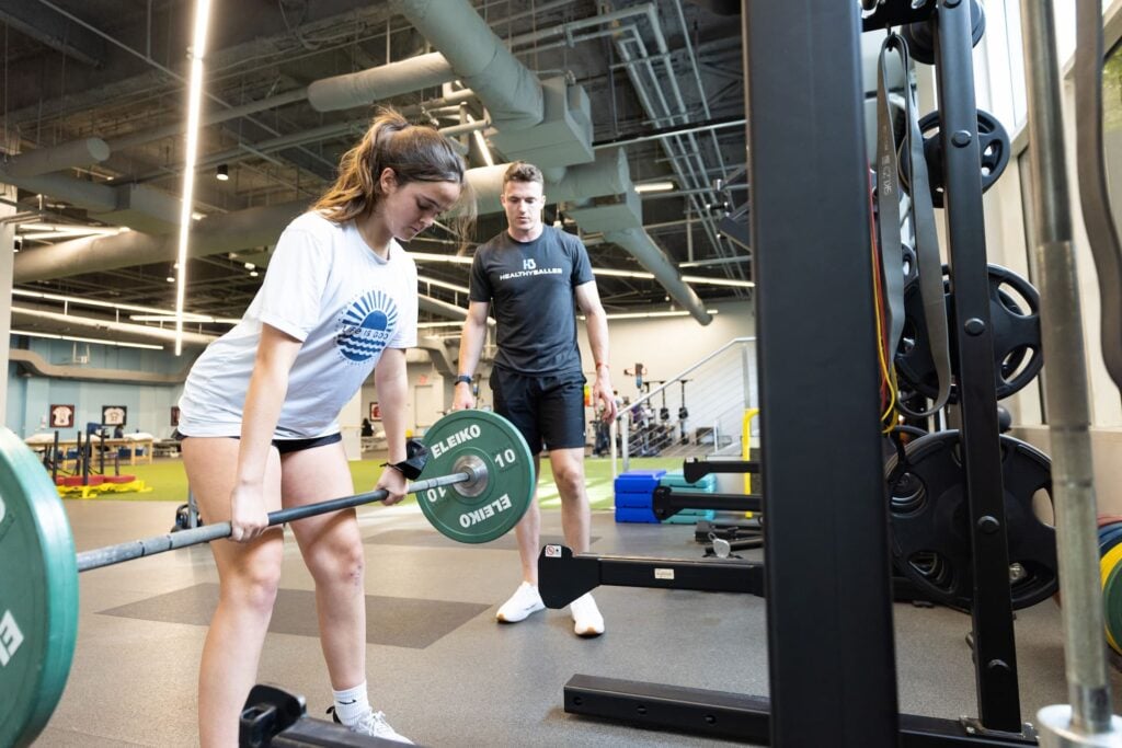 Woman lifting weights with trainer in gym.