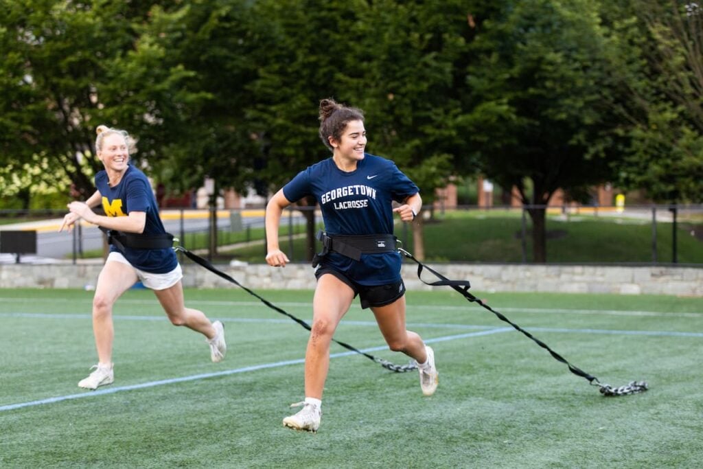 Two athletes training with resistance bands on field.