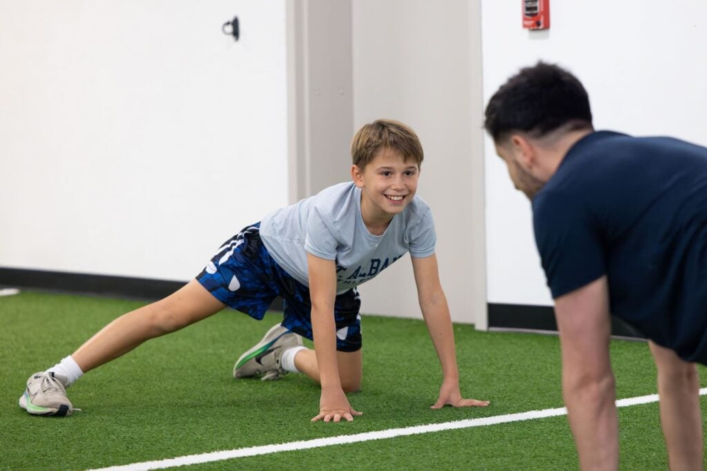 Boy smiling during stretching exercise with coach.