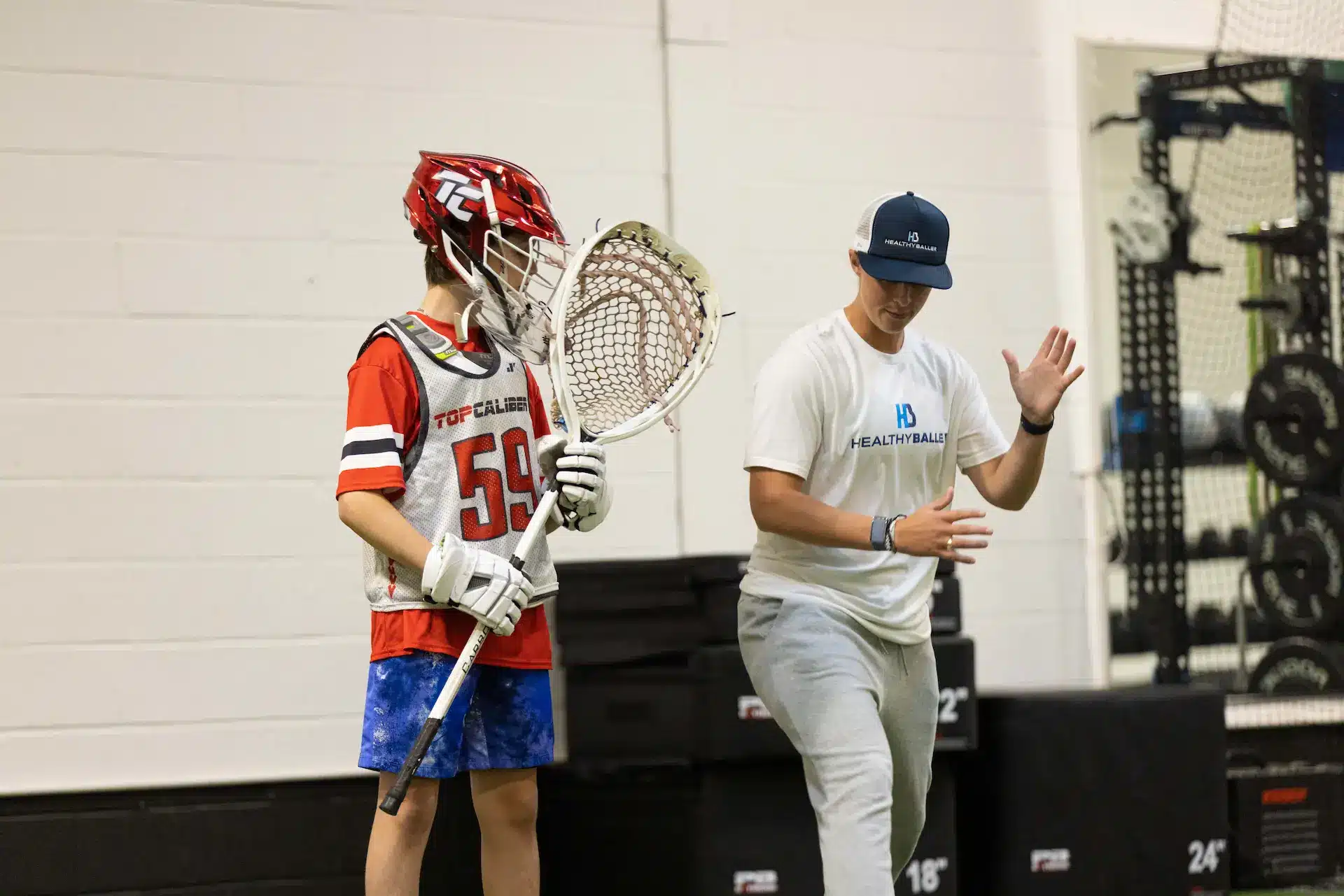 Lacrosse player and coach practicing indoors.