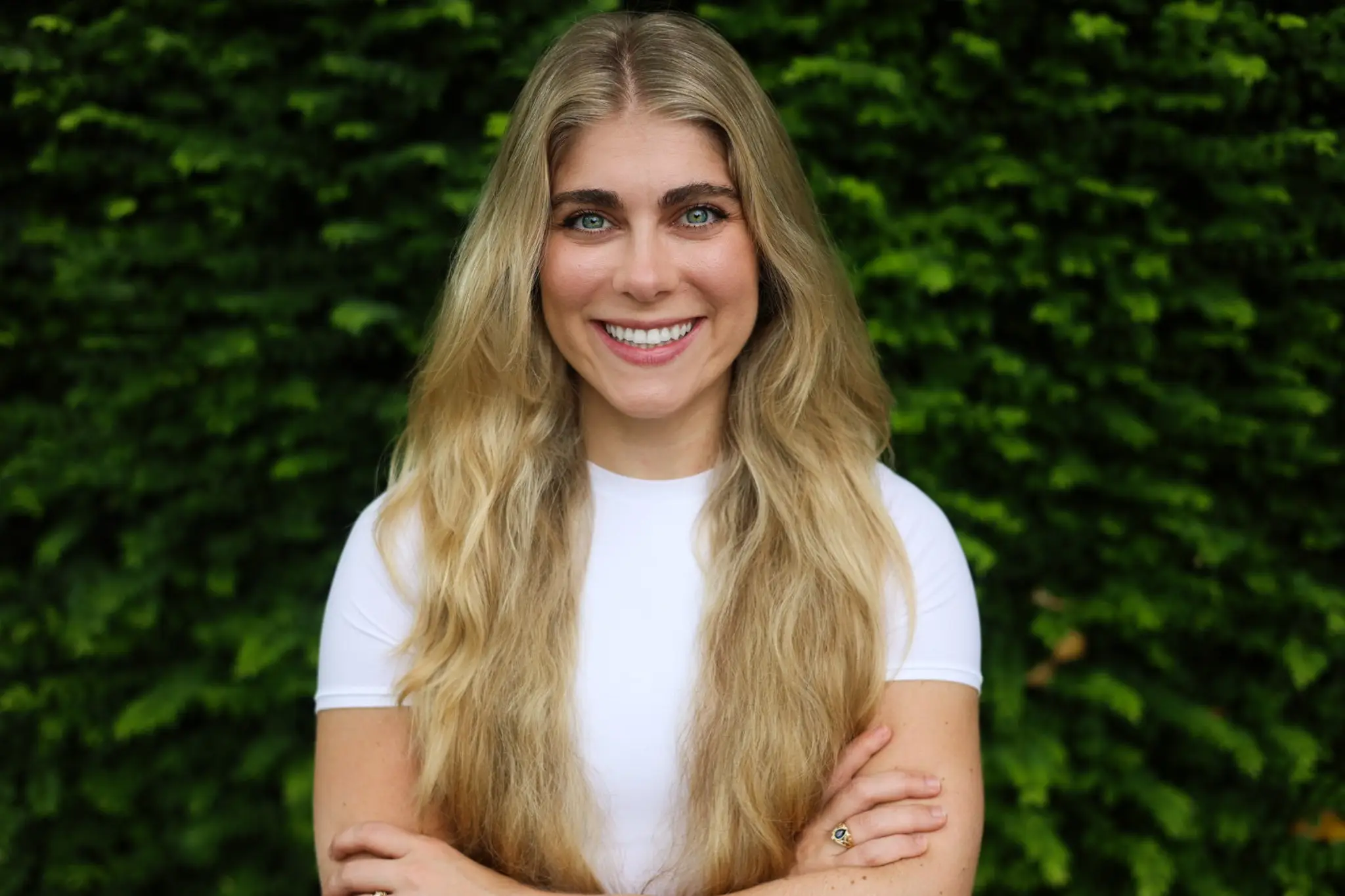 Smiling person with long hair, green leafy background