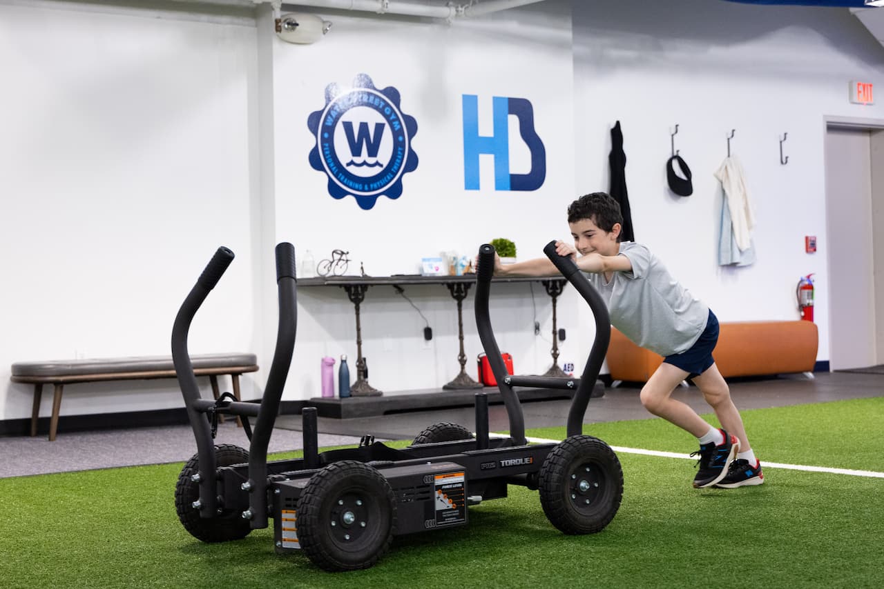Child pushing exercise sled on gym turf