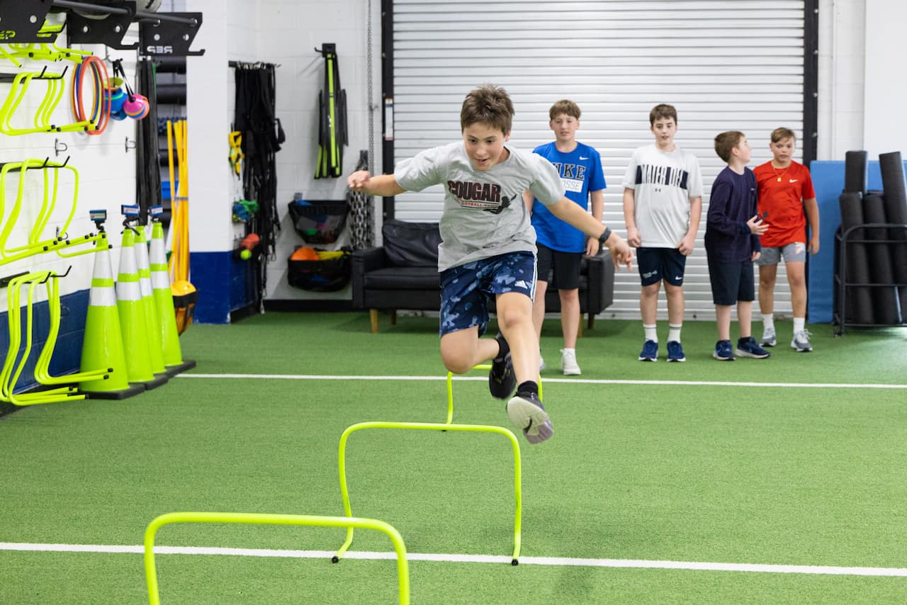 Boy jumping over hurdles in gym class
