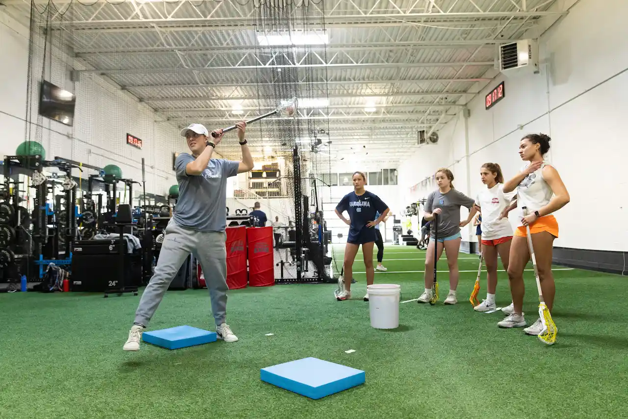 Coach demonstrates swing in indoor lacrosse training session.