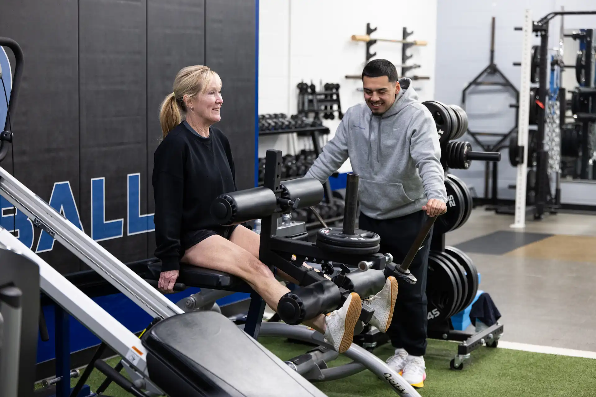Woman exercising on machine at gym with trainer.