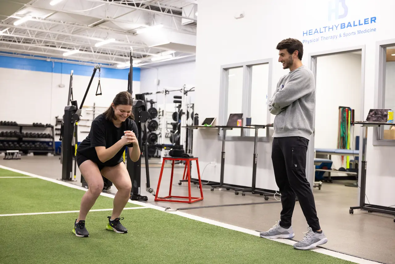 Woman doing squats with trainer in gym.