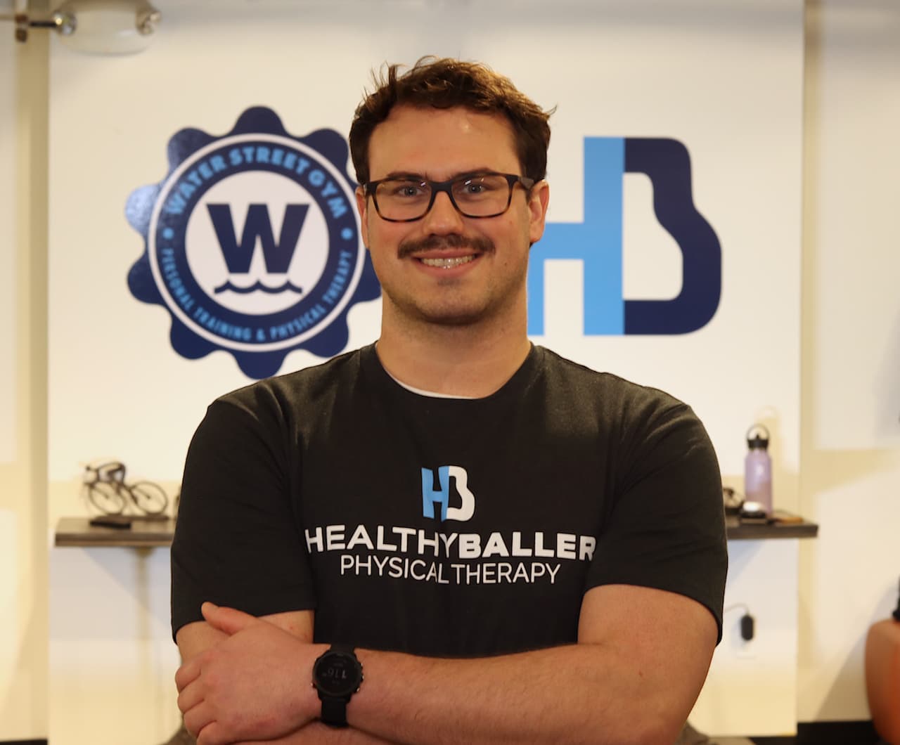 Smiling person stands in gym with folded arms.