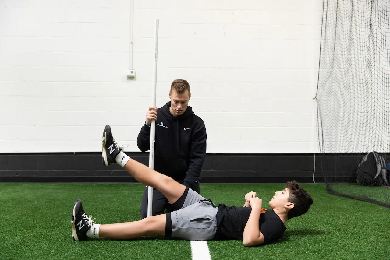 Trainer measuring athlete’s leg raise flexibility indoors