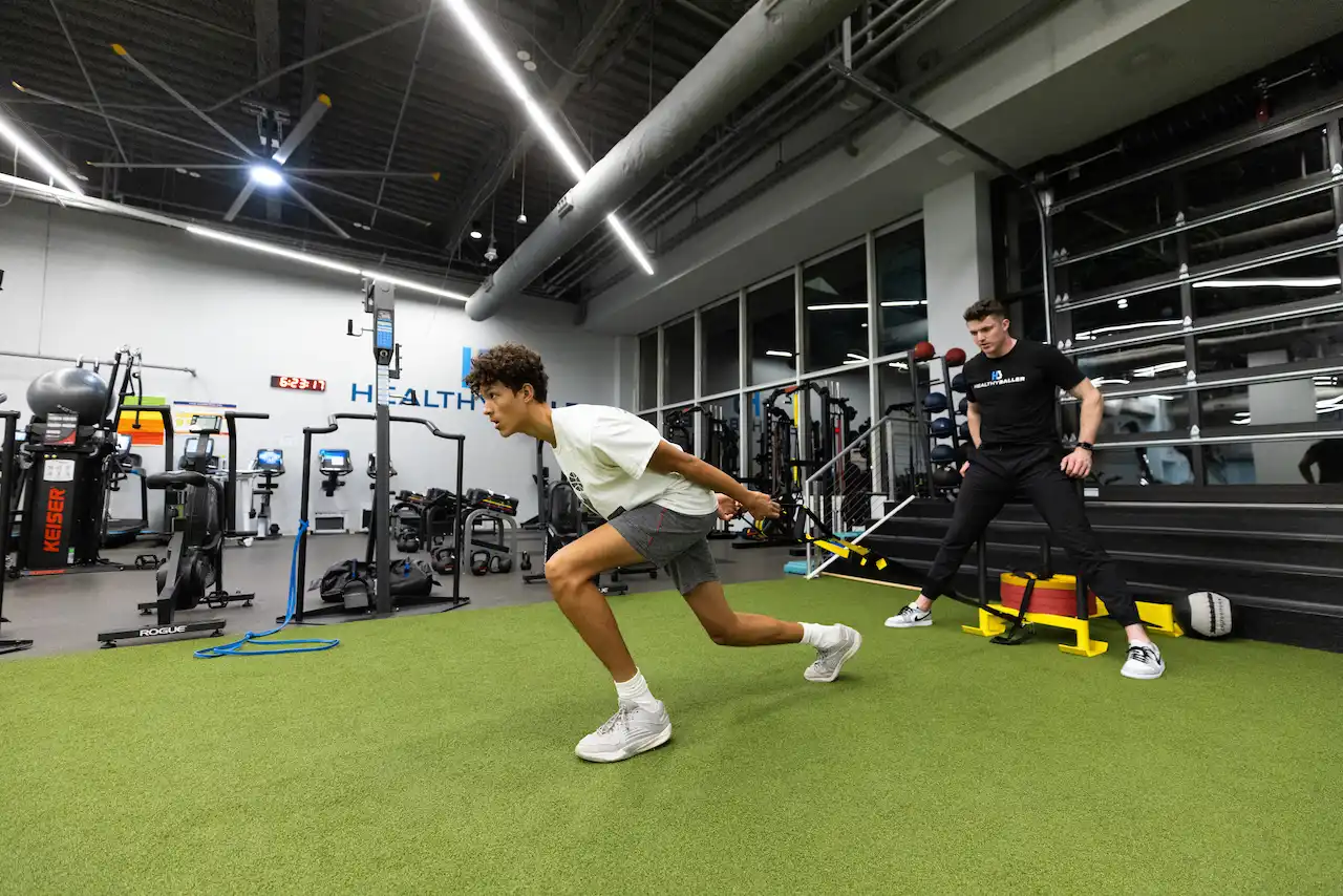 Athlete performs resisted sprint drill with trainer in gym